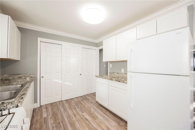 kitchen featuring white cabinets, white refrigerator, light stone countertops, and crown molding