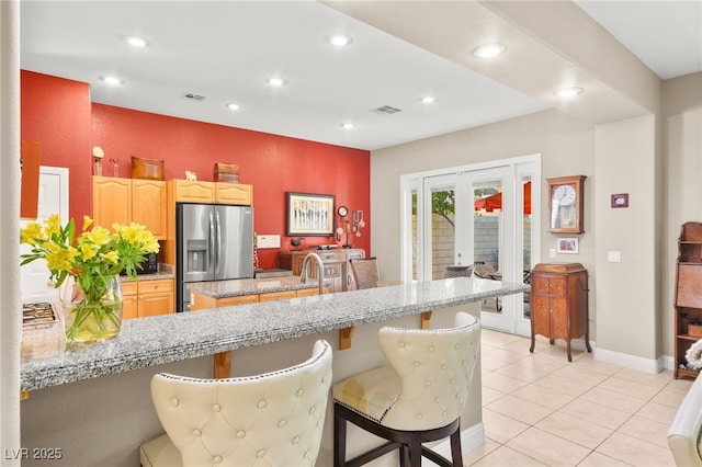 kitchen with stainless steel fridge, light tile patterned floors, light stone counters, a kitchen bar, and kitchen peninsula