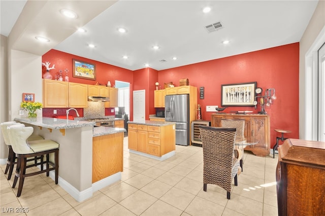 kitchen featuring kitchen peninsula, appliances with stainless steel finishes, a kitchen island, and light brown cabinetry