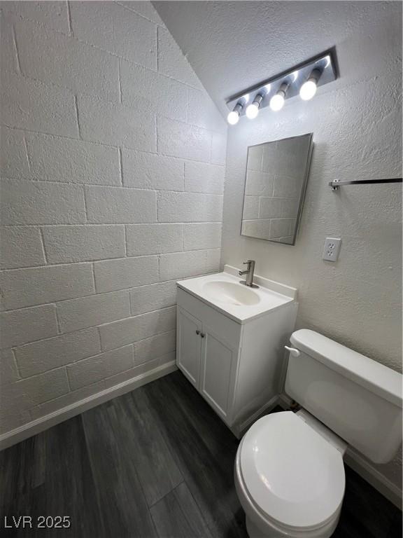 bathroom with wood-type flooring, a textured ceiling, lofted ceiling, toilet, and vanity