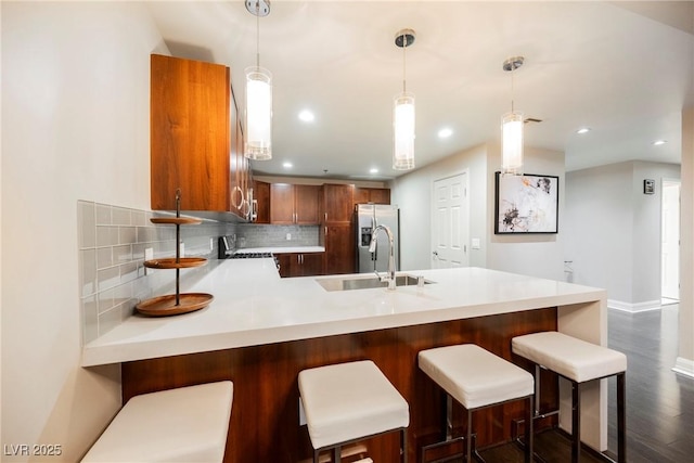 kitchen with pendant lighting, backsplash, sink, stainless steel refrigerator with ice dispenser, and kitchen peninsula