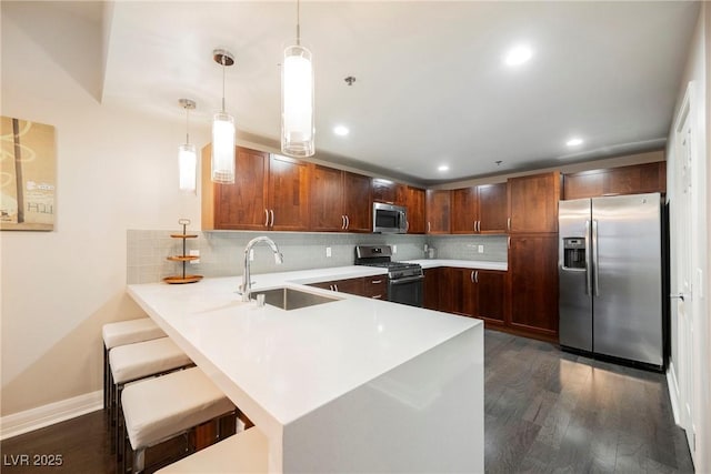 kitchen with sink, stainless steel appliances, dark wood-type flooring, kitchen peninsula, and pendant lighting