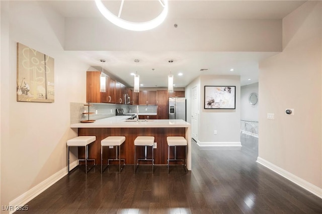 kitchen featuring kitchen peninsula, backsplash, stainless steel appliances, dark hardwood / wood-style floors, and hanging light fixtures