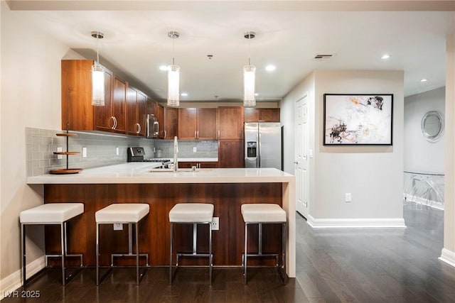 kitchen with kitchen peninsula, appliances with stainless steel finishes, backsplash, a kitchen breakfast bar, and pendant lighting