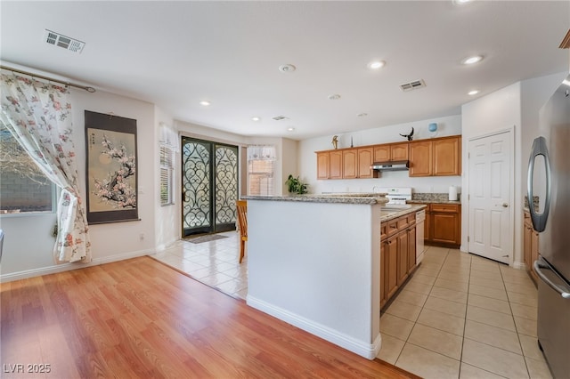 kitchen with stainless steel refrigerator, a center island, range, light tile patterned floors, and light stone countertops