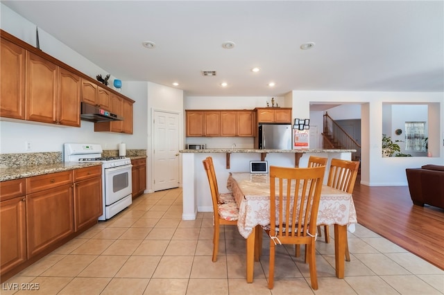 kitchen featuring light tile patterned floors, stainless steel fridge, a kitchen island, a kitchen bar, and white range with gas cooktop