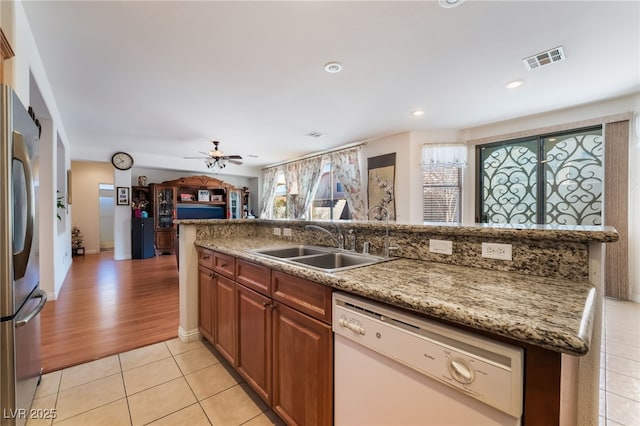 kitchen with sink, light tile patterned floors, stainless steel fridge, dishwasher, and light stone countertops