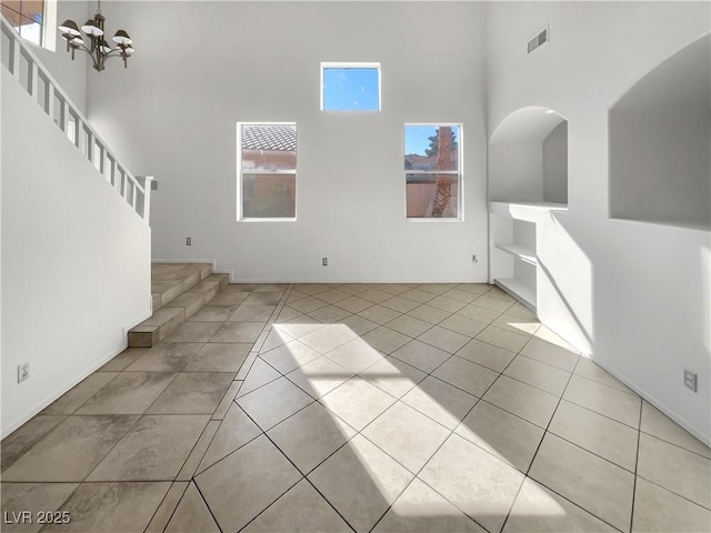 unfurnished living room with light tile patterned floors, a towering ceiling, and a notable chandelier