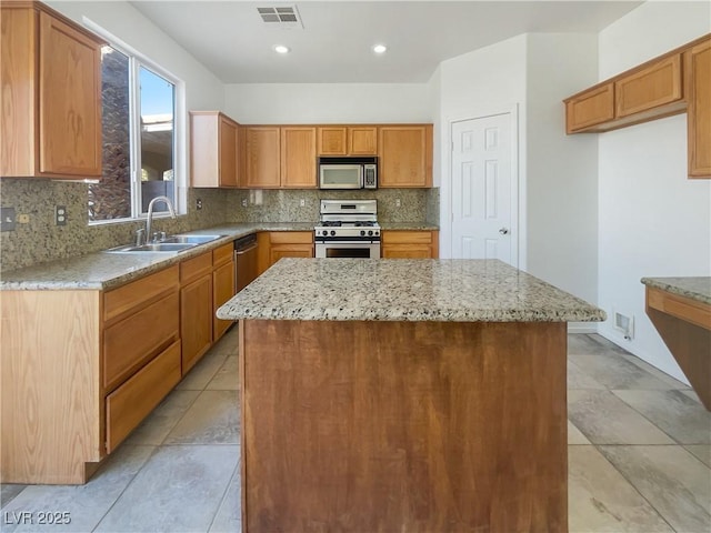 kitchen featuring backsplash, sink, appliances with stainless steel finishes, a kitchen island, and light stone counters