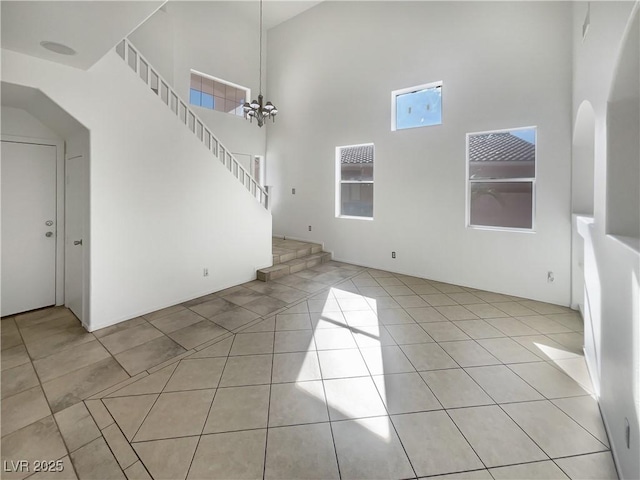 unfurnished living room with light tile patterned floors, a towering ceiling, and an inviting chandelier