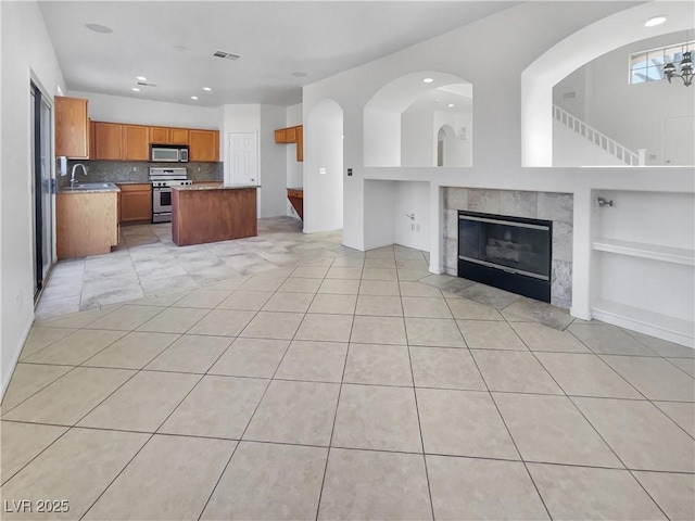 interior space featuring a center island, a tile fireplace, built in shelves, light tile patterned floors, and appliances with stainless steel finishes