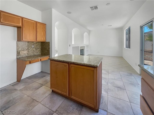 kitchen featuring light stone countertops, light tile patterned floors, backsplash, and a kitchen island