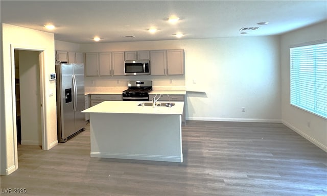 kitchen with a kitchen island with sink, sink, wood-type flooring, and appliances with stainless steel finishes