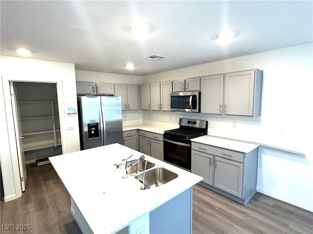 kitchen with gray cabinetry, sink, dark hardwood / wood-style flooring, an island with sink, and appliances with stainless steel finishes