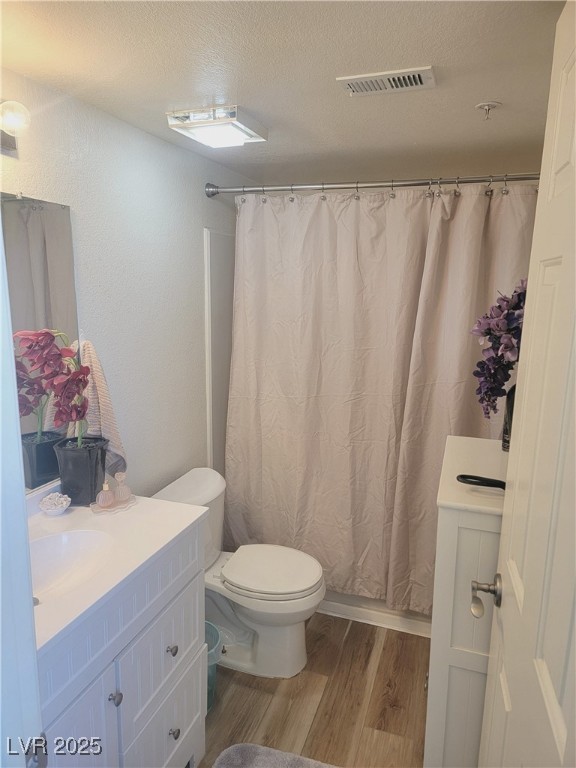 bathroom with toilet, a shower with shower curtain, a textured ceiling, and hardwood / wood-style flooring