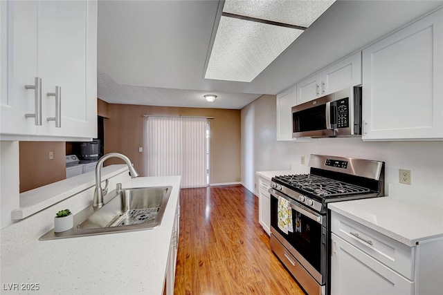 kitchen featuring a skylight, stainless steel appliances, sink, light hardwood / wood-style flooring, and white cabinets