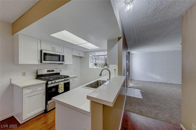 kitchen featuring white cabinetry, sink, stainless steel appliances, brick wall, and kitchen peninsula