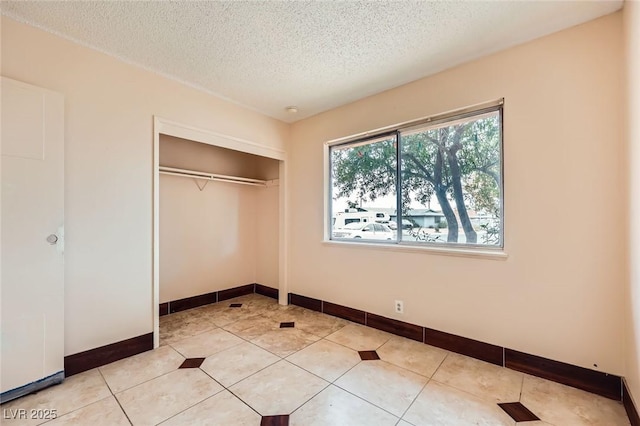 unfurnished bedroom featuring light tile patterned floors, a closet, baseboards, and a textured ceiling