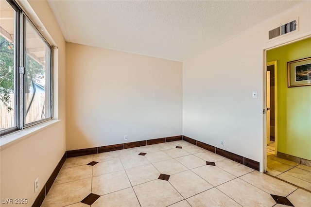 spare room featuring light tile patterned flooring, visible vents, and a textured ceiling