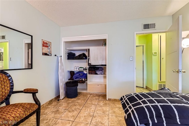 bedroom with light tile patterned flooring, visible vents, a closet, and a textured ceiling