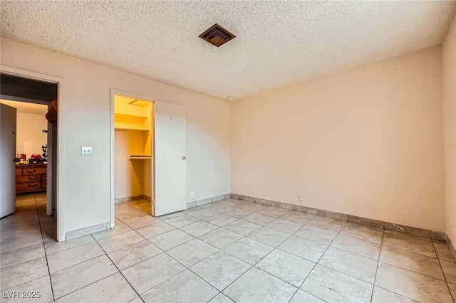 unfurnished bedroom featuring a spacious closet, visible vents, light tile patterned flooring, a closet, and a textured ceiling