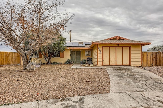 view of front of house with a garage, roof mounted solar panels, driveway, and fence