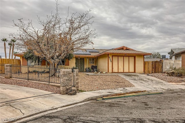 view of front of property featuring a fenced front yard, solar panels, concrete driveway, and an attached garage