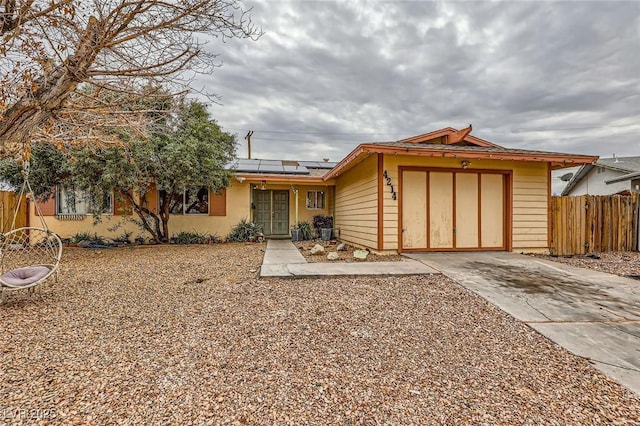 ranch-style home with solar panels, fence, a garage, and driveway