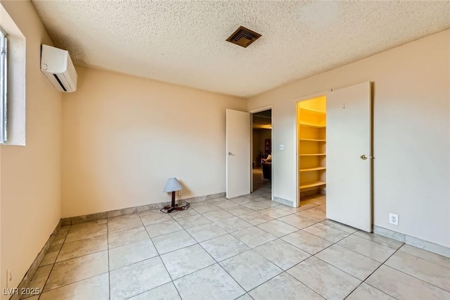 unfurnished bedroom featuring visible vents, a walk in closet, an AC wall unit, a textured ceiling, and light tile patterned floors