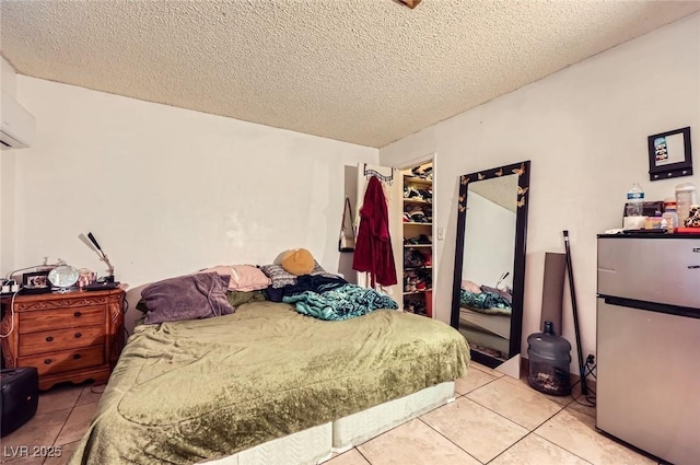 bedroom with a spacious closet, light tile patterned flooring, freestanding refrigerator, and a textured ceiling