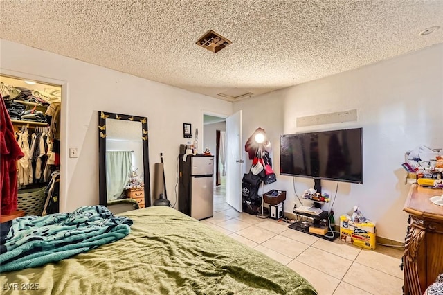 bedroom with visible vents, a walk in closet, freestanding refrigerator, a closet, and tile patterned flooring