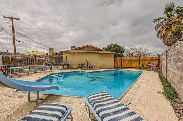 view of swimming pool with a patio, a fenced backyard, a water slide, and a grill