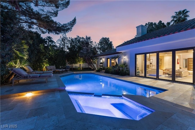 pool at dusk with a patio area and an in ground hot tub