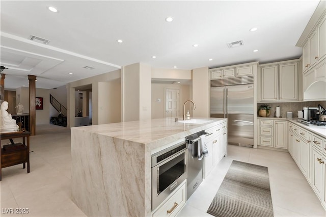 kitchen featuring cream cabinetry, stainless steel appliances, light stone countertops, and sink