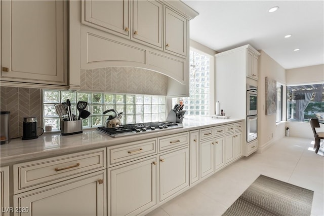 kitchen featuring stainless steel appliances, light stone counters, cream cabinetry, decorative backsplash, and light tile patterned floors