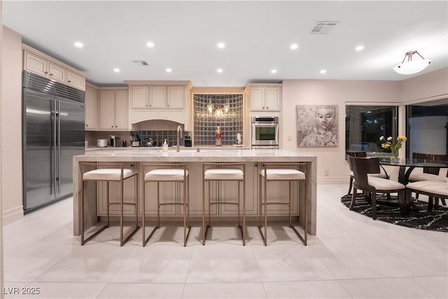 kitchen with appliances with stainless steel finishes, tasteful backsplash, a breakfast bar, a kitchen island with sink, and light tile patterned floors