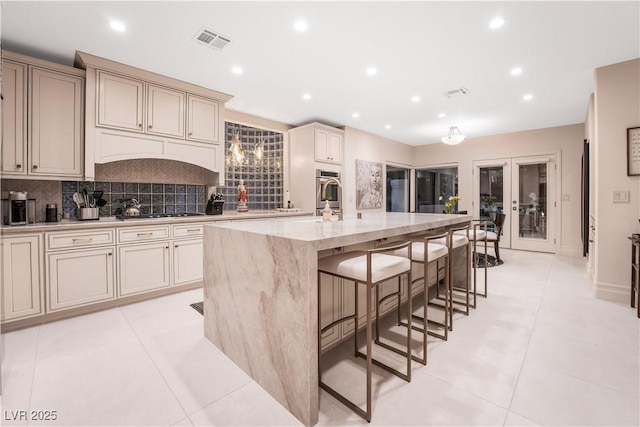 kitchen featuring a kitchen breakfast bar, a kitchen island with sink, cream cabinets, and stainless steel oven