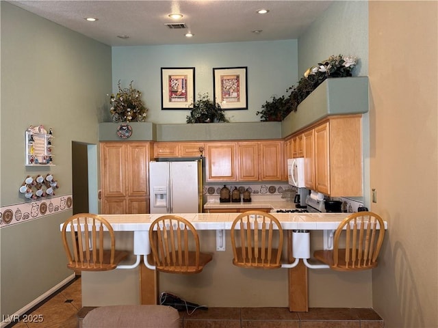 kitchen with a kitchen breakfast bar, kitchen peninsula, light tile patterned floors, and white appliances