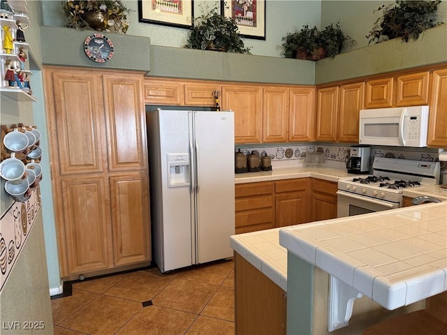 kitchen with kitchen peninsula, white appliances, tile counters, and light tile patterned flooring