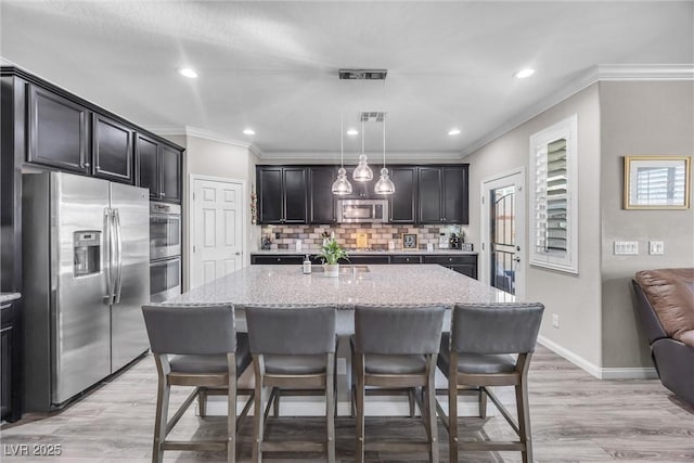 kitchen with decorative light fixtures, light stone counters, stainless steel appliances, and a kitchen island with sink