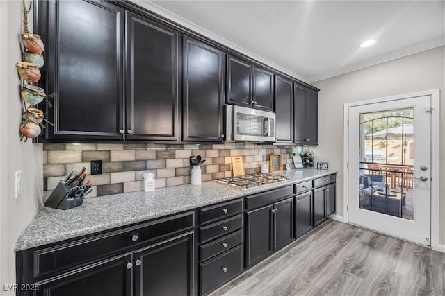 kitchen with light stone countertops, backsplash, stainless steel appliances, crown molding, and light hardwood / wood-style floors