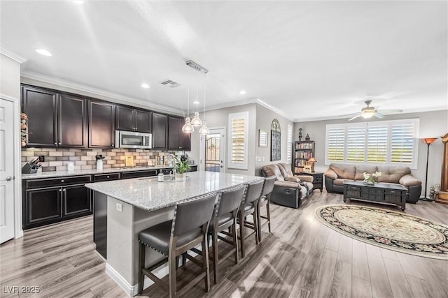 kitchen with light stone countertops, backsplash, pendant lighting, a breakfast bar area, and an island with sink