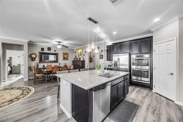 kitchen featuring stainless steel appliances, ceiling fan, sink, pendant lighting, and an island with sink