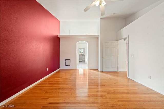 empty room featuring a high ceiling, light wood-type flooring, and ceiling fan