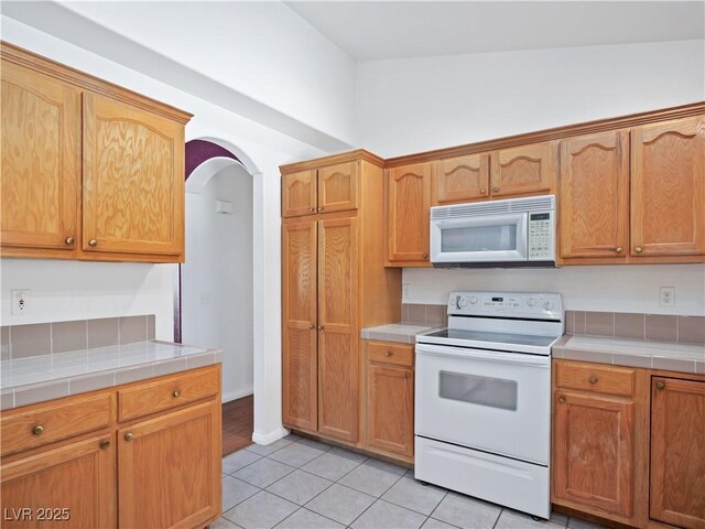 kitchen featuring light tile patterned floors, white appliances, and tile countertops