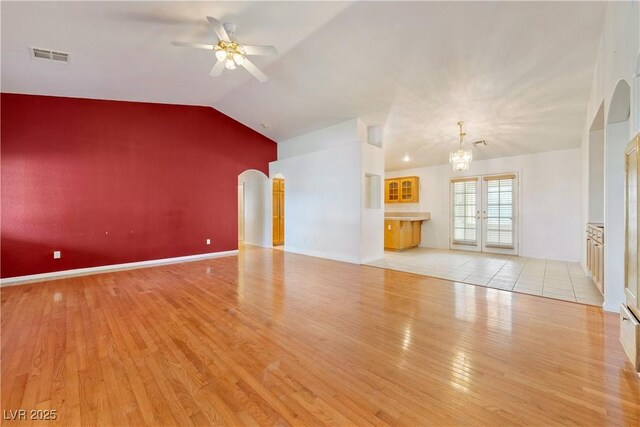 unfurnished living room featuring ceiling fan with notable chandelier, light hardwood / wood-style floors, french doors, and vaulted ceiling