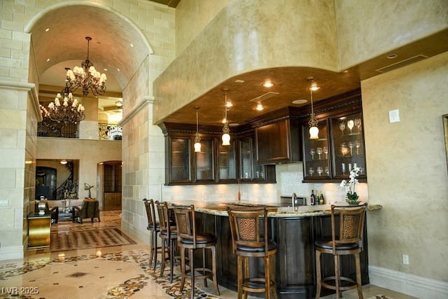 bar with light stone counters, brick ceiling, dark brown cabinetry, pendant lighting, and lofted ceiling