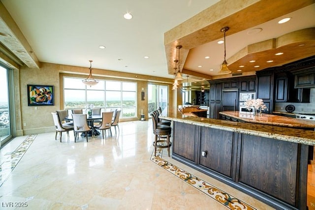 kitchen featuring light stone countertops, dark brown cabinets, built in appliances, and hanging light fixtures