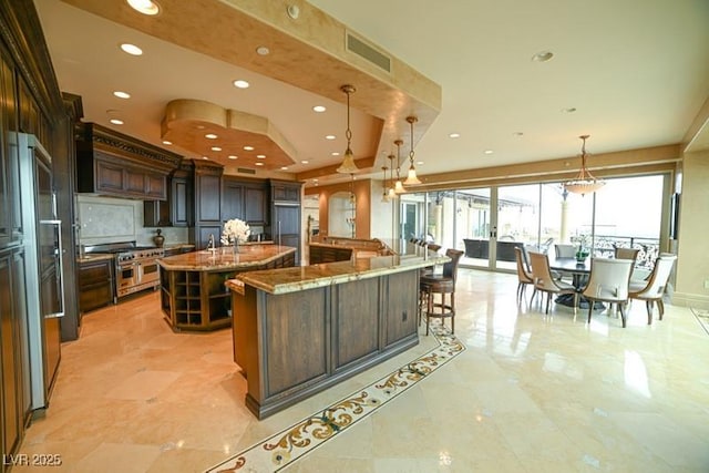 kitchen featuring dark brown cabinetry, stone counters, a large island, decorative light fixtures, and appliances with stainless steel finishes