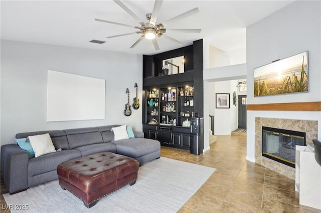 living room with a tile fireplace, bar, and ceiling fan